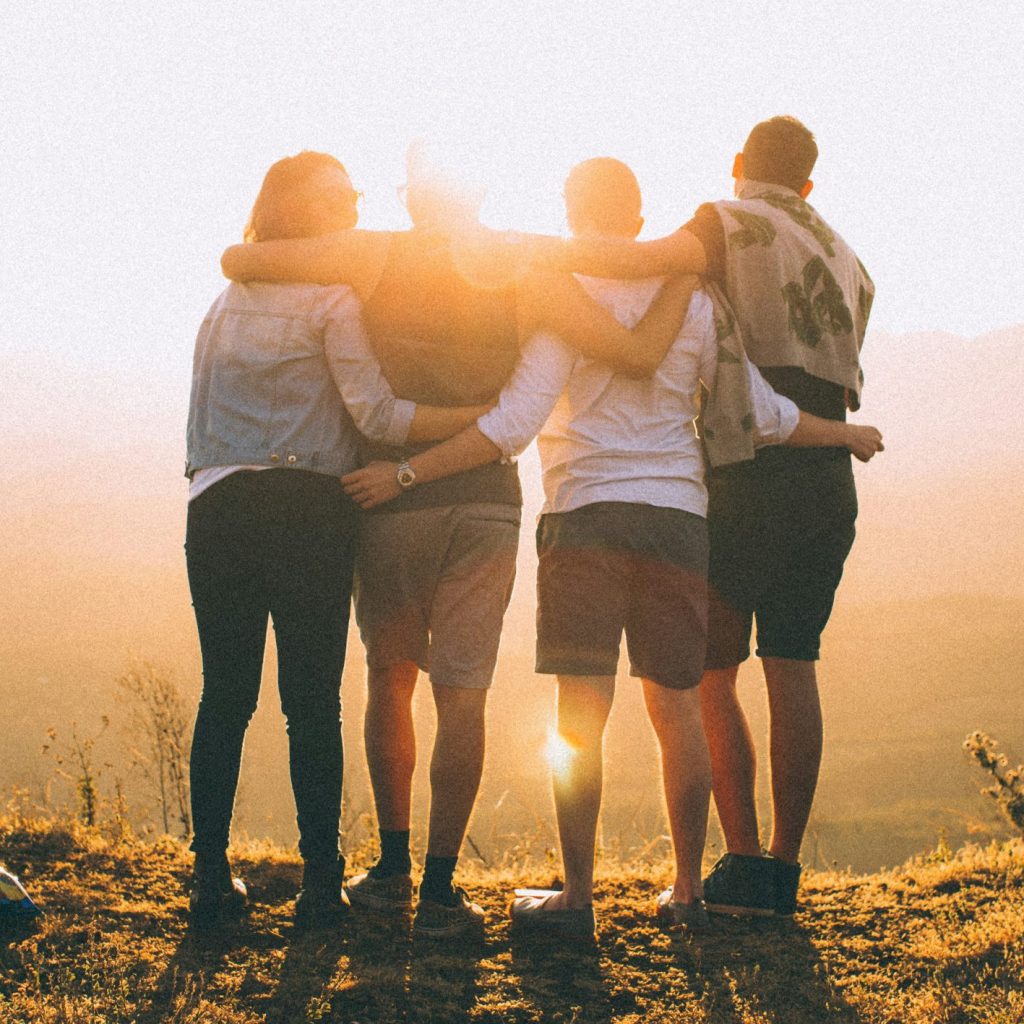 Groupe de 4 personnes au coucher du soleil qui se serrent les unes contre les autres